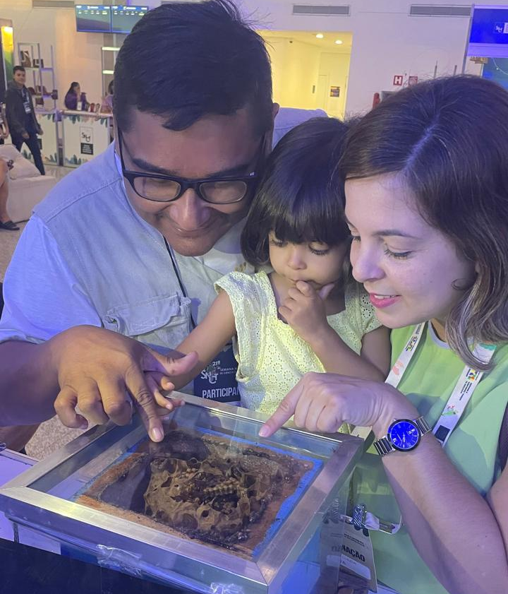 Richardson Frazão mostrando uma colmeia fechada a uma criança e uma mulher